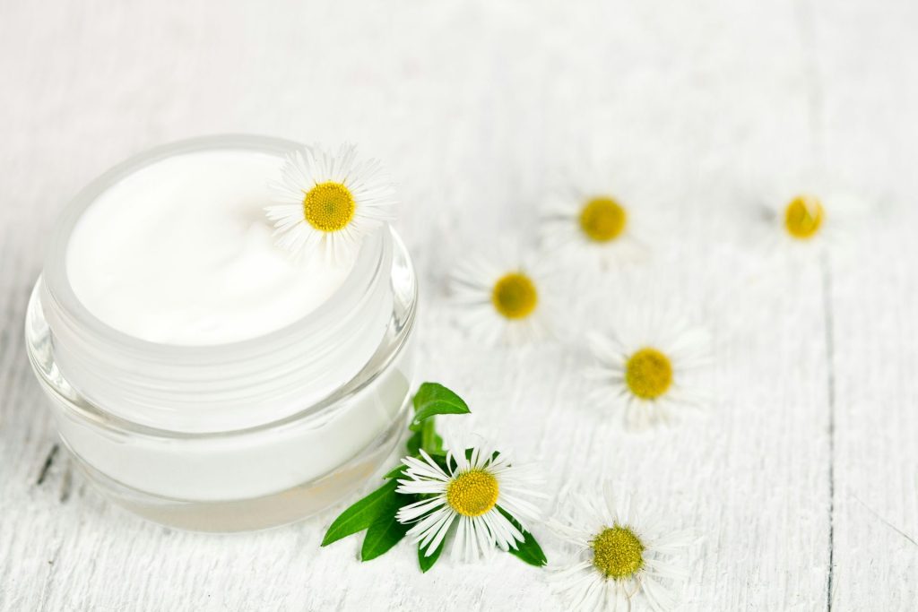 A jar of cream with daisies on a white wooden table